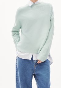 Pull tricot vert menthe clair à coupe ample, texture côtelée et épaules tombantes, porté sur une chemise blanche à col.