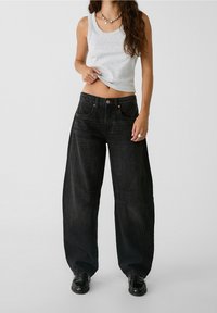 Szerokie czarne dżinsy denimowe z wysokim stanem, z miedzianymi guzikami i wypranym wykończeniem. W zestawie z szarym topem na ramiączkach.