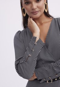 Czarna i biała bluzka w paski z długimi rękawami, z dodatkiem złotych guzików i dekoltem w kształcie litery V. Materiał ma gładką teksturę.