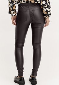 Leggings en simili cuir marron avec une coupe slim, dotés de deux poches arrière et d'une texture lisse, associés à des chaussures à plateforme noires.