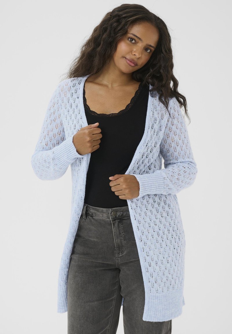 Hellblau offener Strickcardigan mit langen Ärmeln, gerippten Bündchen und lockerer Passform, kombiniert mit einem schwarzen Tanktop und grauen Hosen.