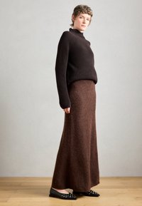 Maglione a coste marrone scuro abbinato a una lunga gonna marrone con texture. Ballerine nere con dettagli in metallo argentato. Silhouette semplice e moderna.