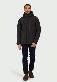 Giacca isolante nera con zip frontale, cappuccio regolabile e due tasche frontali. Presenta una texture morbida e un design aderente.