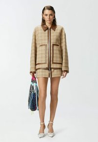 Tamno karirani sako s smešnim kožnim detaljima, s rajsferšlusom i dva prednja džepa, uparen s odgovarajućim mini suknjom i šarenom torbom.