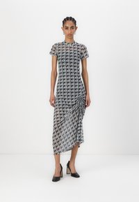Sheer black and white midi dress with geometric pattern, round neckline, short sleeves, and side ruching detail, paired with black heels.