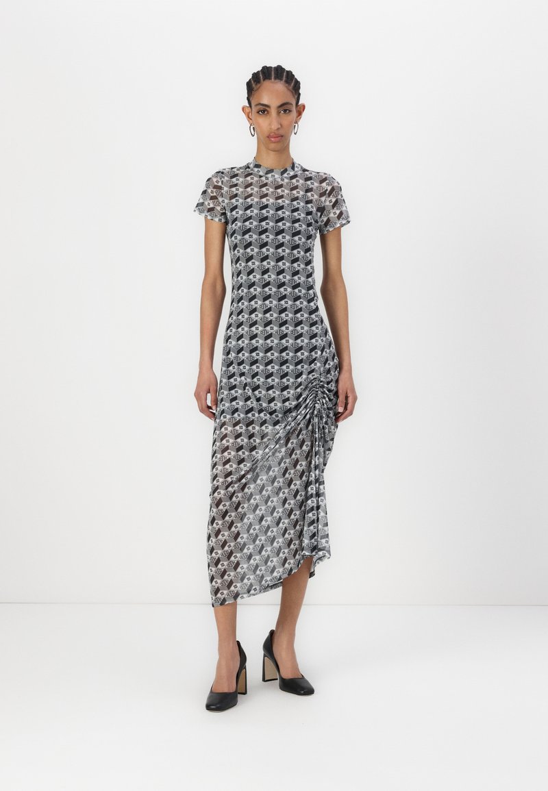 Sheer black and white midi dress with geometric pattern, round neckline, short sleeves, and side ruching detail, paired with black heels.