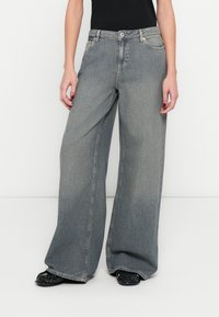 Széles szárú, szürke farmernadrág magasított derékkal, gombos és cipzáras záródással, elöl zsebekkel, enyhén kifakult textúrával.