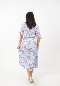 Lichtblauwe bloemenjurk met korte mouwen, strikdetails en een vloeiende silhoutte. Bevat kleurrijke bloemenpatronen over de hele jurk.