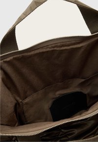 Hnědá textilní taška uvnitř s hladkým povrchem, vybavená zipem a černou etikettou. Podšívka je v mírně světlejším hnědém odstínu.