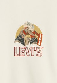 Maglietta bianca con un'illustrazione retrò di due cowboy, con il logo "LEVI'S" in rosso acceso e pois bianchi in basso.