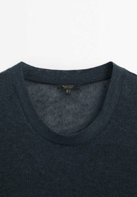 Pull tricoté gris foncé avec un col rond et une étiquette de marque visible à l’intérieur du col.