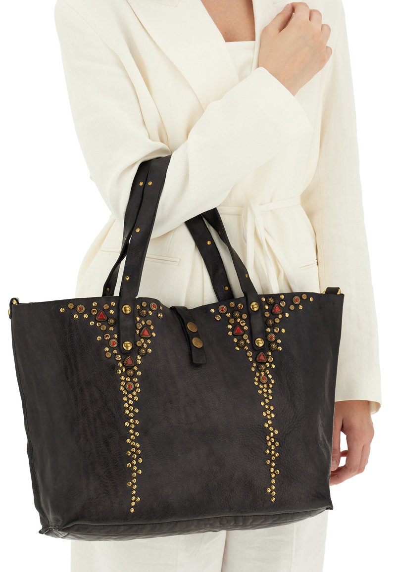 Borsa tote in pelle nera con borchie decorative dorate e rosse, dotata di manici doppi e forma strutturata.