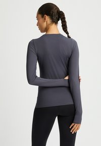 Dunkelgraues, langärmeliges Sportoberteil mit strukturiertem Muster, figurbetontem Schnitt, rundem Halsausschnitt und verlängerten Bündchen, kombiniert mit schwarzen Leggings.