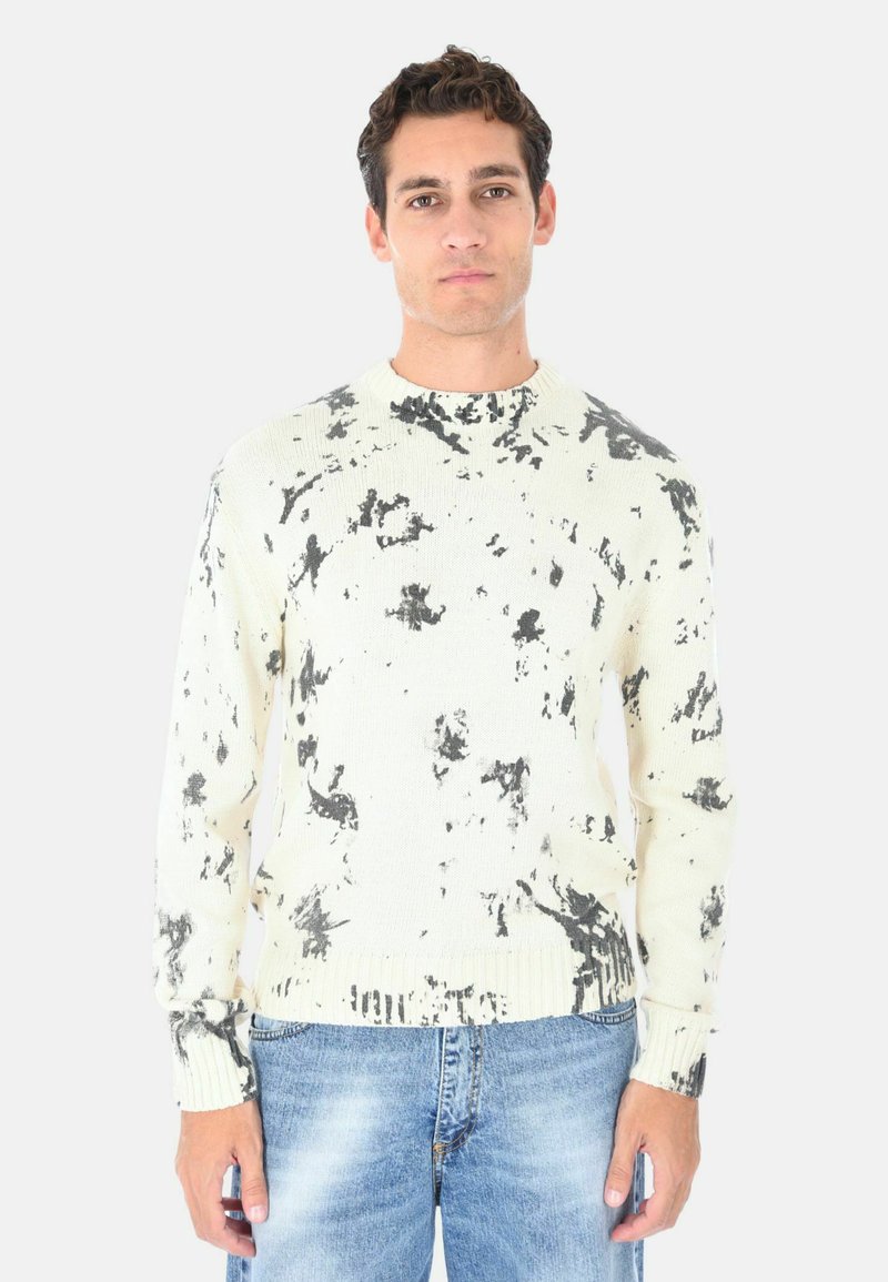 Maglione di maglia color crema con un motivo astratto nero, scollo a girocollo e polsini e orlo a coste. Abbinato a jeans blu chiaro.