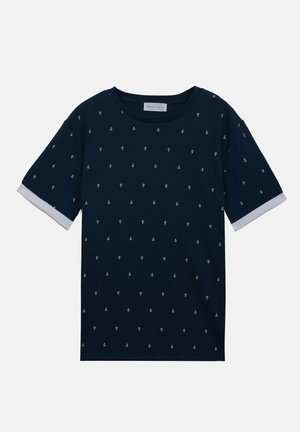 T-shirt à manches courtes bleu marine avec petits motifs d'ancres blanches et poignets blancs aux manches, col rond, vue en plongée sur fond blanc.
