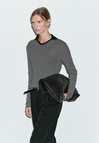 Black and white striped long-sleeve top with a V-neck, paired with high-waisted black trousers, holding a textured black bag.