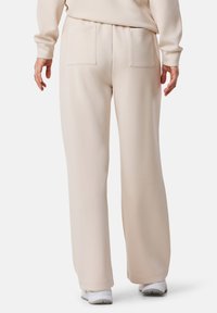 Beige sweatpants met een ruime fit, voorzien van twee achterzakken en een gladde textuur, gecombineerd met witte sportschoenen.
