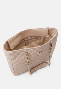 Sac fourre-tout synthétique beige matelassé avec des poignées en chaîne dorée et une poche zippée à l'intérieur, doté d'une doublure en tissu à motifs et d'un détail de logo.