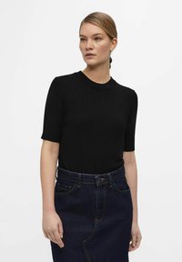 Sort ribbet striktrøje med korte ærmer og rund halsudskæring. Sammen med en højttalende denimnederdel med synlig søm.