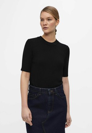 Svart ribbad stickad tröja med korta ärmar och rund hals. Tillsammans med en högmidjad denimkjol med synliga sömmar.