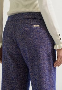 Hose mit blauem und braunem Fischgrätmuster und hohen Taillen, mit einem kleinen Etikett auf der Gesäßtasche und weichem Material.
