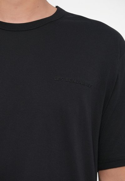 T-shirt nera a maniche corte in tessuto liscio con logo in rilievo "LES BENJAMINS" sul petto. Collo a giro e vestibilità rilassata.