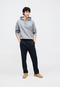 Hall hall kapuutsiga dressipluus eest tasku ja reguleeritavate nööridega, kombineeritud mustade jooksupükstega. Komplekti lõpetavad beežid tossud.