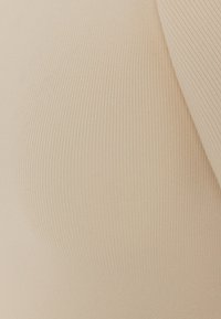 Beige ribbet stoff som viser vertikale linjer med en jevn tekstur; delvis synlig erme antyder en tettsittende design.