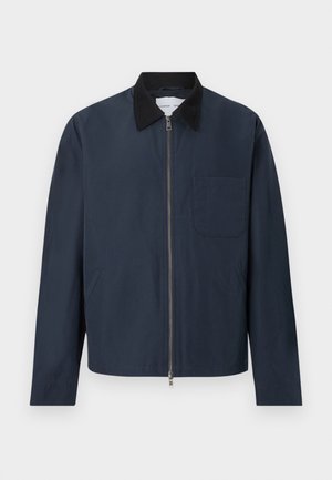 Jachetă bleumarin cu fermoar, guler negru, mâneci lungi, două buzunare laterale și un buzunar pe piept pe partea stângă.