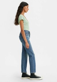 Green ribbed top with short frilly sleeves, high-waisted blue jeans, and black high-top sneakers, viewed from the side.