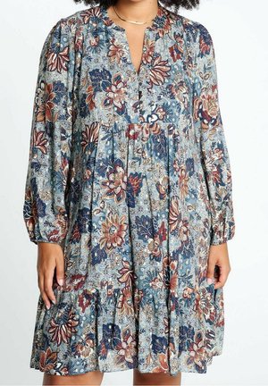 Robe à manches longues à motif floral bleu, rouille et beige, avec un décolleté en V et une taille froncée portée par une personne à la peau moyennement foncée.