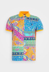Färgglad polo skjorta med en blandning av blommönster och geometriska mönster i orange, blått och rosa. Den har en enfärgad orange krage och korta  ärmar.
