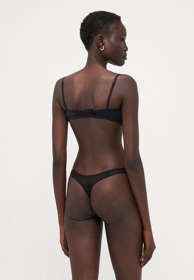 Ensemble de lingerie noire comprenant un soutien-gorge lisse avec des bretelles réglables et un string transparent assorti avec des bordures en dentelle, vu de l'arrière.