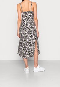 Svart blomster midi-klänning med tunna remmar, prydd med lila och gula blommor, en sidoklyfta och en flödande silhuett. Bärs med vita sneakers.