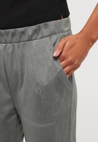 Grijze suède broek met een gladde textuur en zijzakken, met een relaxte pasvorm en rekbare tailleband. Hand in de zak gepositioneerd.