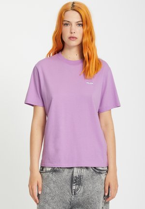 T-shirt en coton lavande avec un col rond et des manches courtes, arborant un petit motif blanc sur la poitrine gauche. Texture lisse.
