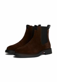 Stivali Chelsea in camoscio marrone con pannelli elastici neri ai lati e linguette. Tacco basso con un'accensione di colore a contrasto sulla suola.