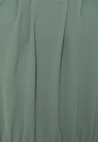 Gestructureerde salie groene stof met subtiele verticale plooien en een iets verheven geweven patroon.