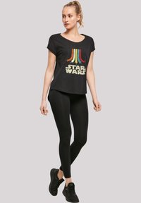 Juodas trumpas rankovėmis marškinėliai su daugiakomponentine Star Wars grafika, derinami su juodais leggingais ir juodais sportiniais batais.