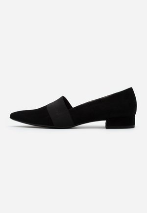 Chaussure noire à talon bas et bout pointu, à enfiler, avec une large sangle élastique traversant le médio-pied, présentée sur un fond clair uni.