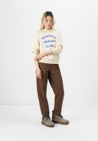 Hanorac crem cu text albastru, pantaloni negri și cizme gri. Îmbrăcămintea are o croială lejeră și culori contrastante. Design simplu și stil practic.