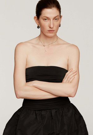 Vestido negro sin mangas con un corsé ajustado y falda acampanada, hecho de un tejido texturizado; collar plateado y grandes pendientes circulares.