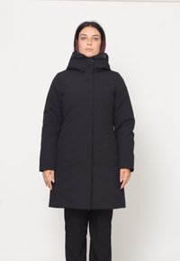 Parka nera lunga con colletto alto e cappuccio. Presenta un taglio dritto, maniche lunghe e tasche laterali. Texture liscia e opaca.