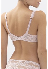 Vaaleanpunainen pitsinen liivi, jossa on kukkakuviot, säädettävät olkaimet ja hakasuljenta takana. Pehmeä rakenne ja hienovaraiset yksityiskohdat.