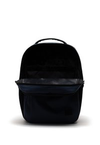 Zaino in tessuto blu scuro con forma arrotondata, maniglia superiore e tasca in rete all'interno del compartimento principale. Nessun dettaglio esterno visibile.