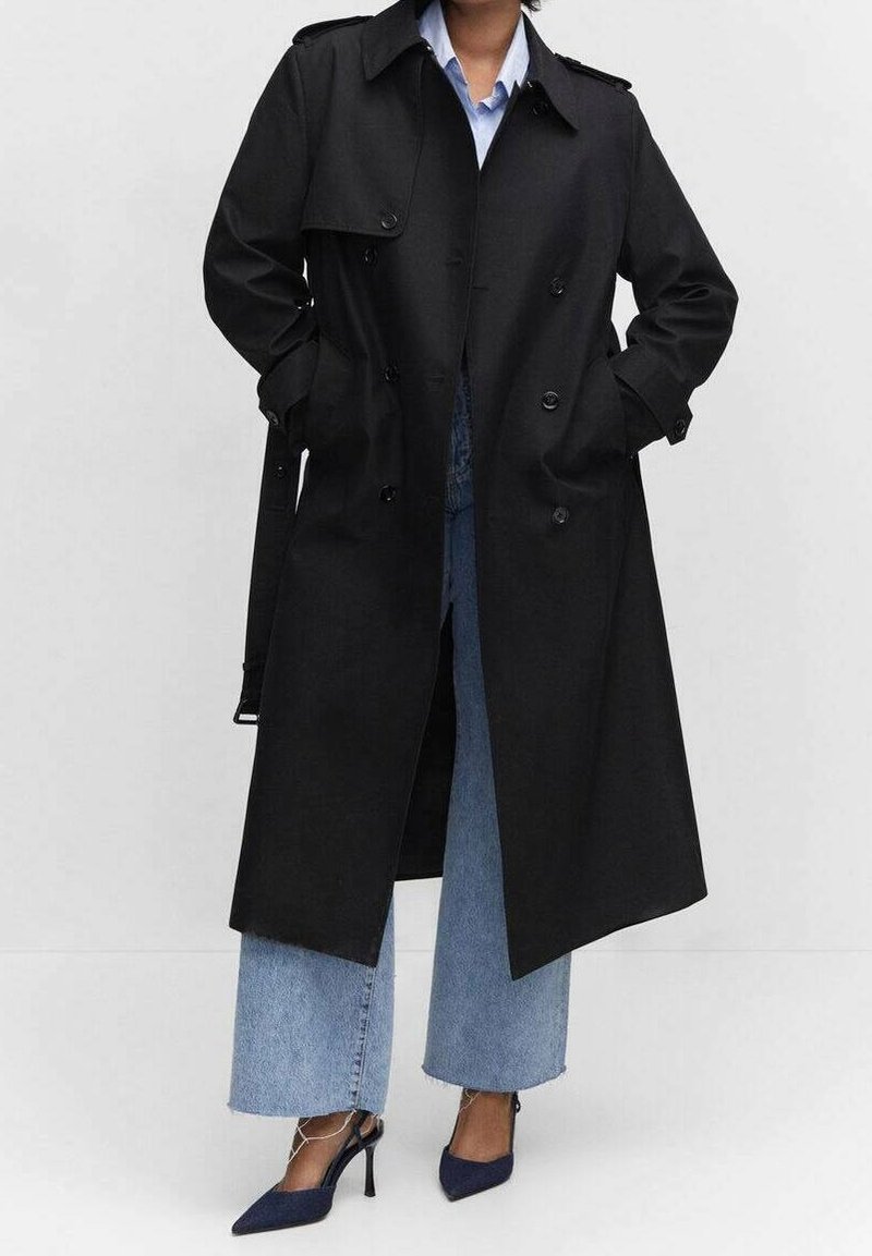 Czarny płaszcz trencz o fasonie dwurzędowym, z dużymi klapami, pagonami na ramionach i bocznymi kieszeniami, noszony na jasnoniebieskiej koszuli i dżinsach.
