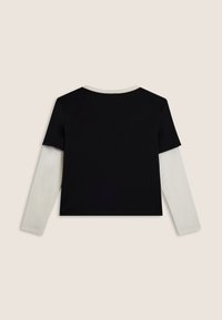 Top nero a maniche corte sovrapposto a una camicia bianca a maniche lunghe, con scollo rotondo e finiture dorate sul colletto.