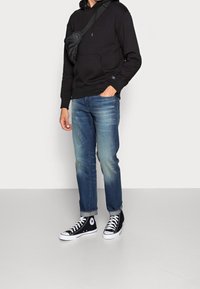 Černá mikina s kapucí a přední kapsou, modré slim-fit džíny a černé vysoké tenisky s bílou podrážkou a logem.