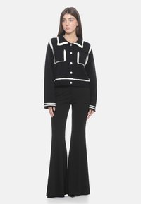 Maglione cropped nero con dettagli bianchi, grandi bottoni e due tasche frontali. Abbinato a pantaloni neri a campana.
