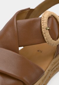 Καφέ σανδάλι από συνθετικό δέρμα με πλεγμένο λουράκι σε ταμπά απόχρωση, διακοσμημένο με στρογγυλή αγκράφα και σόλα πλατφόρμας με υφή.